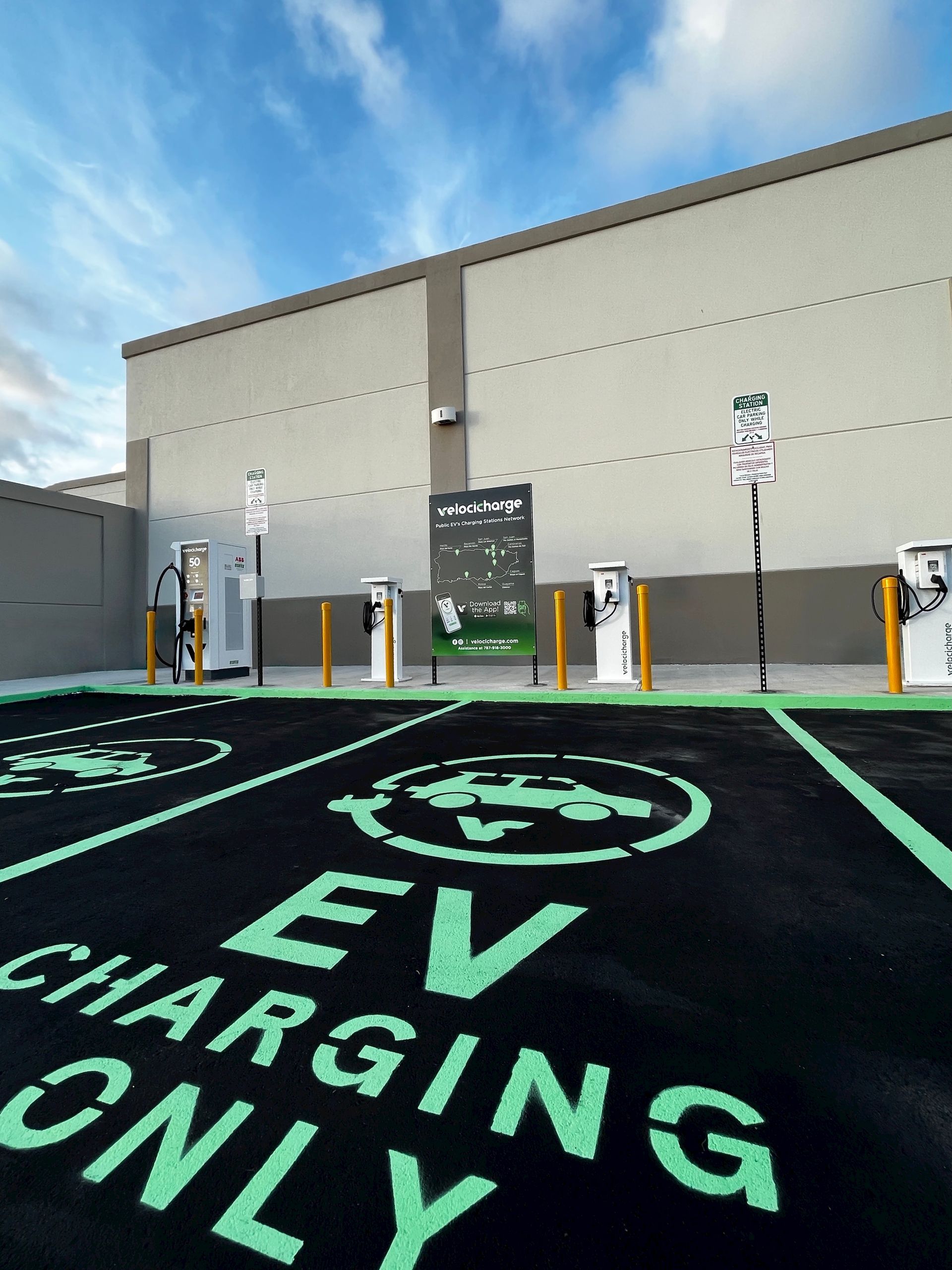 Electric vehicle charging station; green markings on asphalt, charging stations, and building in background.