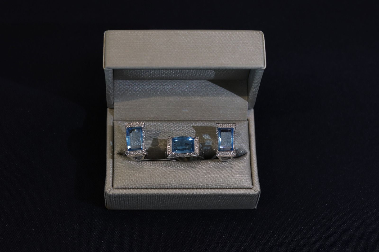 A pair of cufflinks and a ring in a box on a black background.