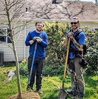 Two men are standing next to each other in a yard holding shovels.