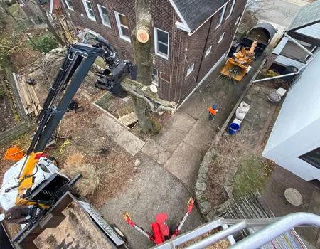 Aerial view of a house exterior with excavation machinery and workers in a narrow driveway beside a brick building.