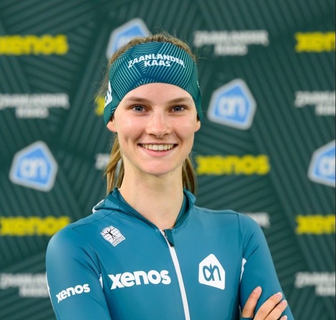 Lachende wielrenner in een turquoise Xenos-teamshirt en -hoofdband, staand voor een achtergrond van de sponsor.