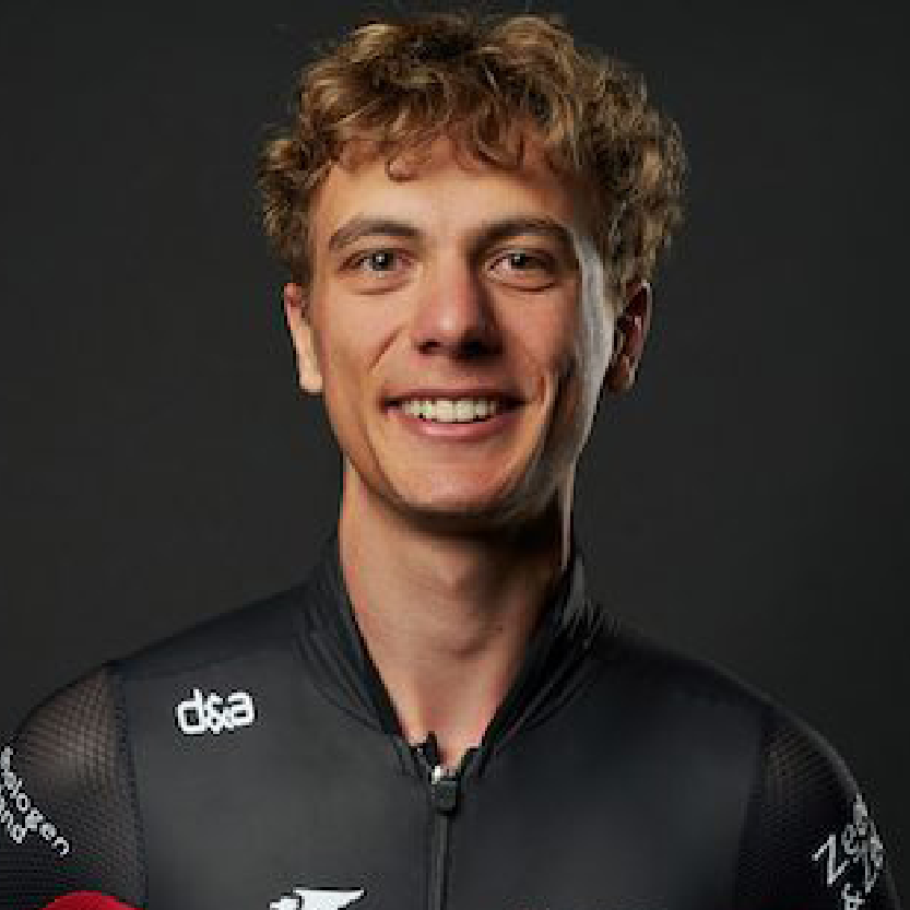 Lachende wielrenner in een zwart shirt tegen een donkere achtergrond.