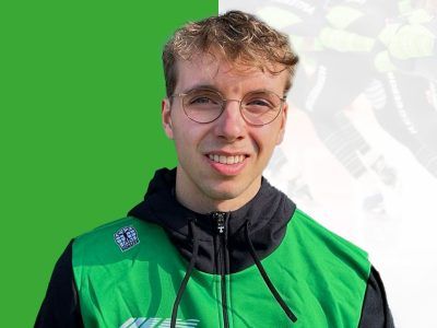 Persoon met bril en groene jas lacht tegen een felgroene achtergrond.