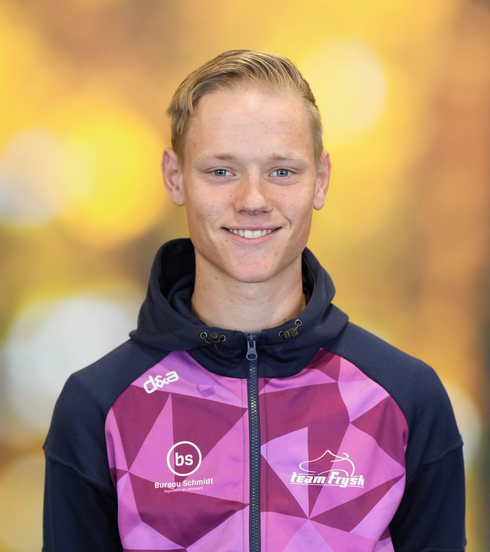 Lachende atleet in een paarse sportjas met rits tegen een wazige gouden achtergrond.