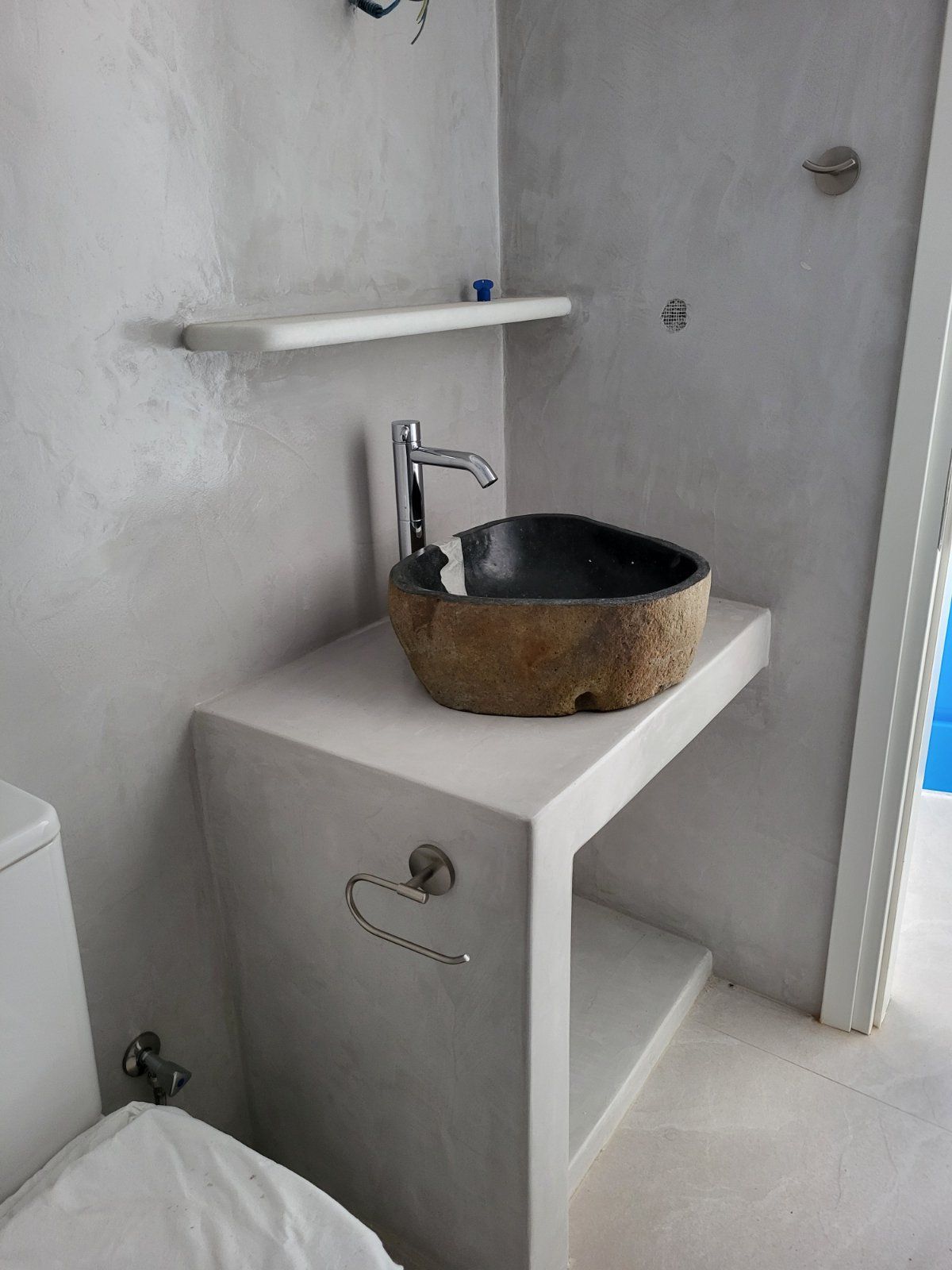 Bathroom with a stone sink on a white counter. Gray walls and a shelf.