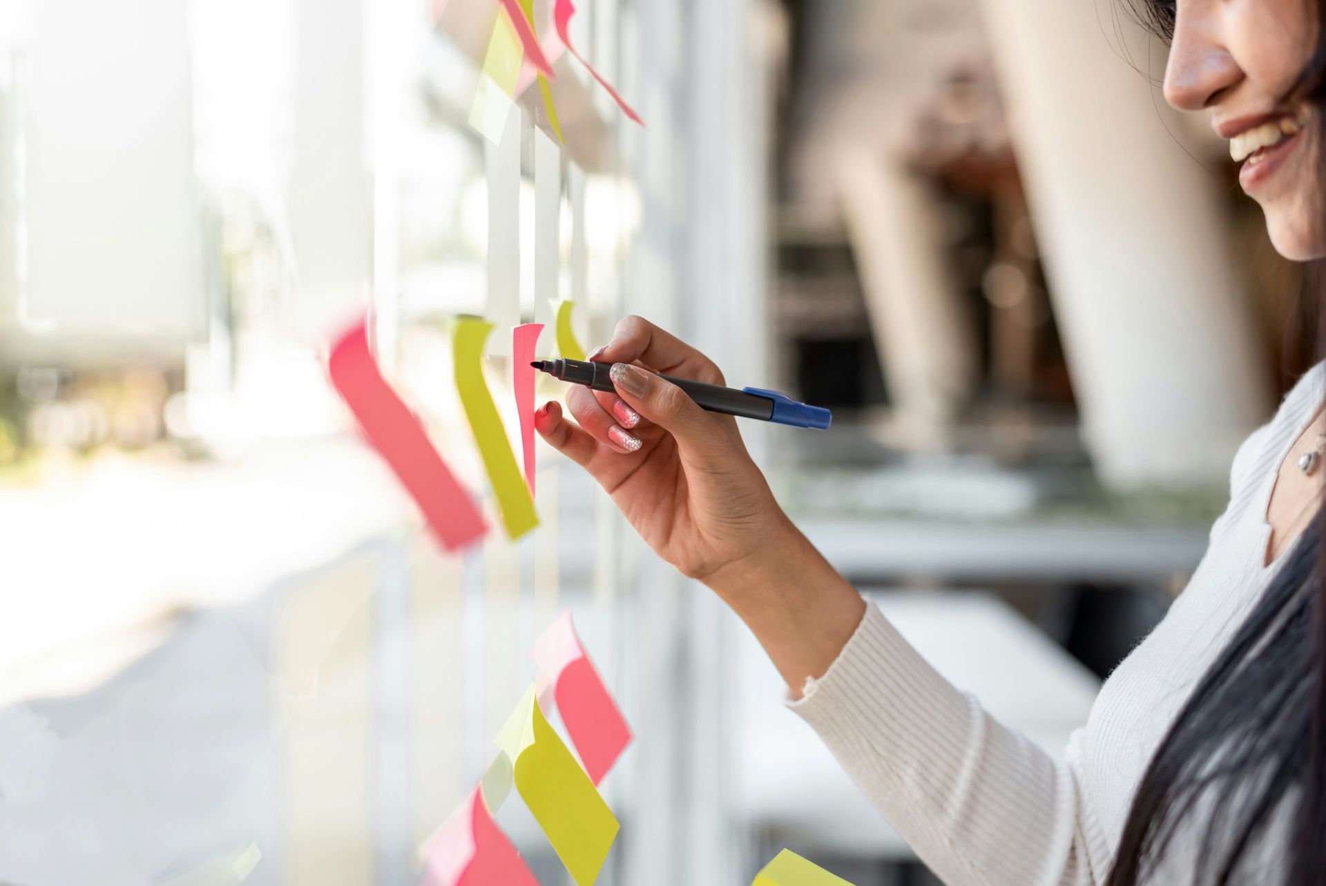 Woman writes on sticky note on window with bright sunlight.