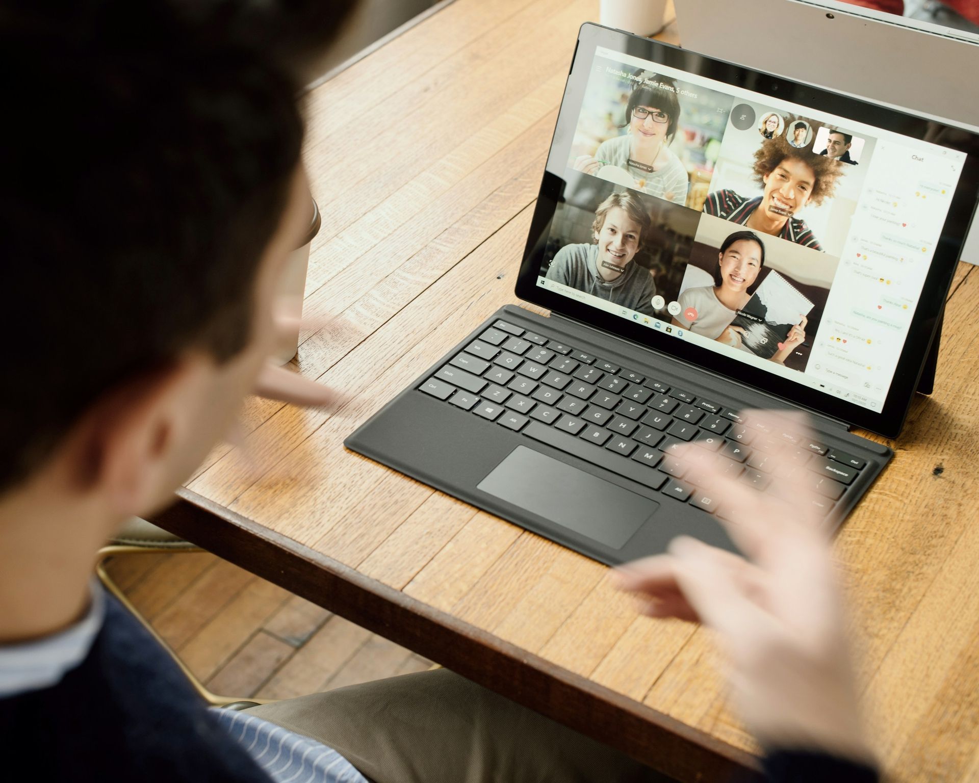 Person gestures during video call on a laptop. Group of people on screen in a home office setting.