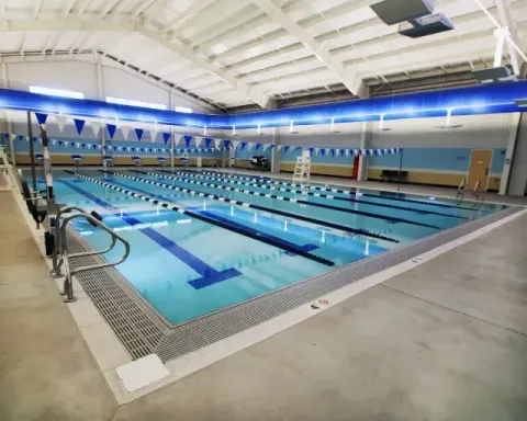 Indoor swimming pool with multiple lap lanes, blue water, and white ceiling lights