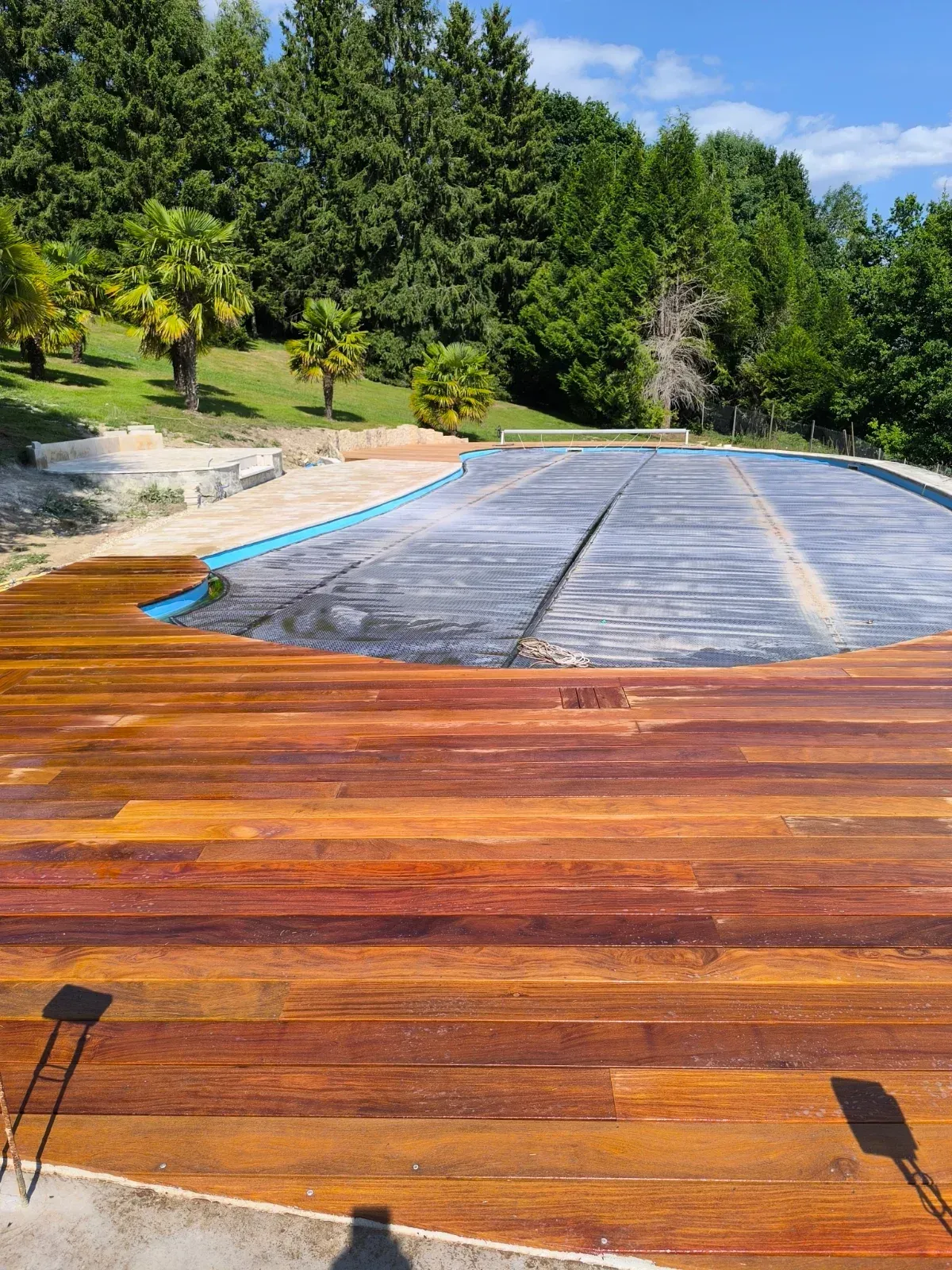 Plage de piscine en bois exotique en cours de saturation, vue sur les palmiers