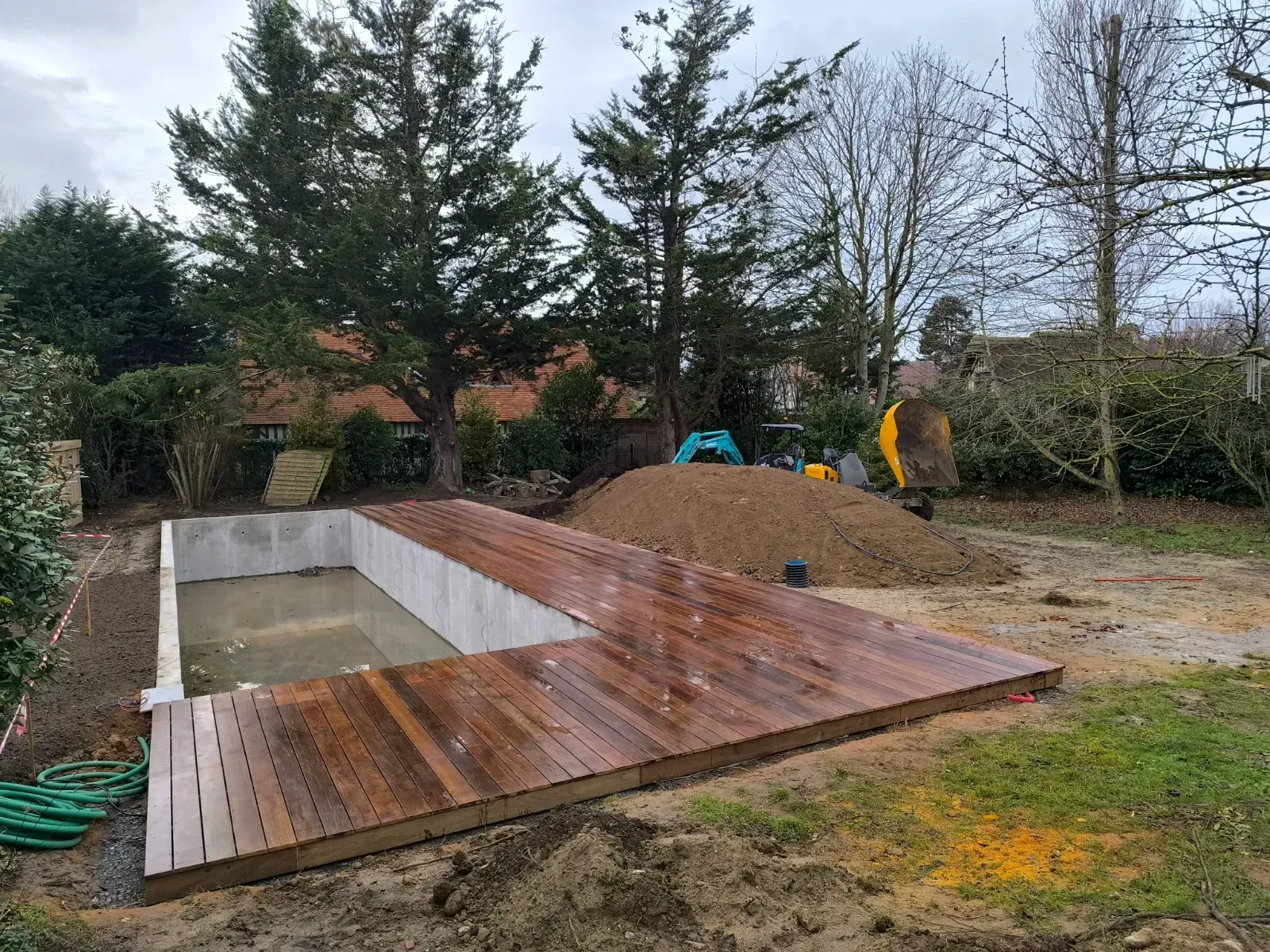 Avant : coque de piscine en béton brut, plage en bois en cours de pose en hiver