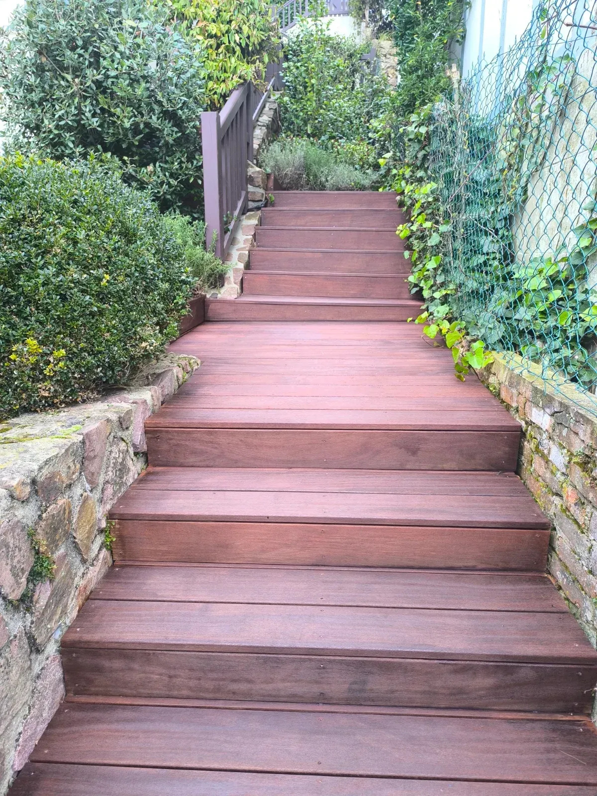 Escalier extérieur en bois exotique avec garde-corps le long d'un mur de pierre