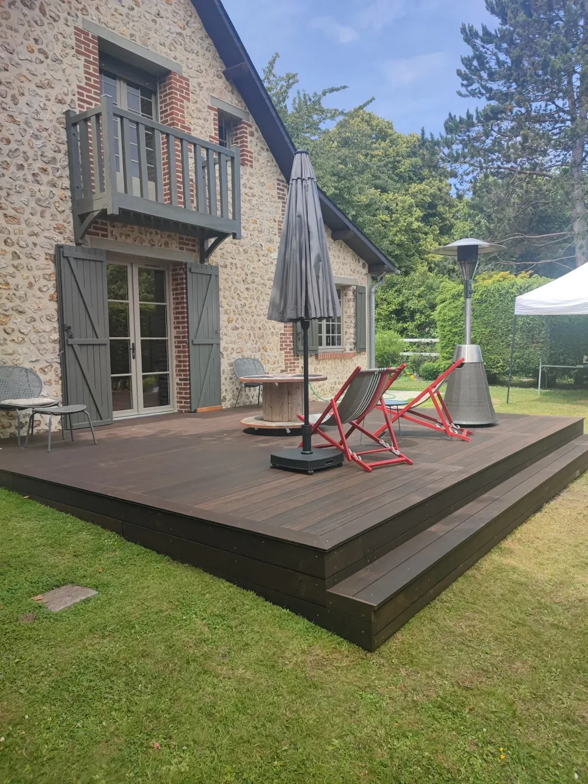 Terrasse en bois exotique foncé devant une maison en pierre et brique