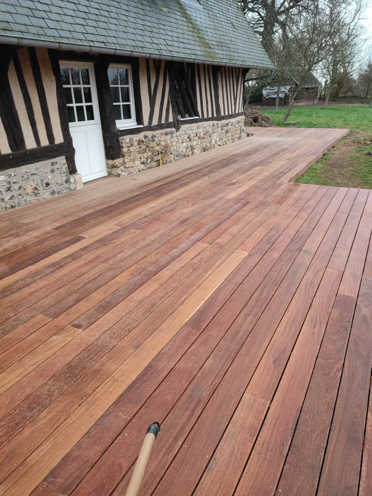 Terrasse en bois exotique le long d'une maison normande à colombages et soubassement en silex