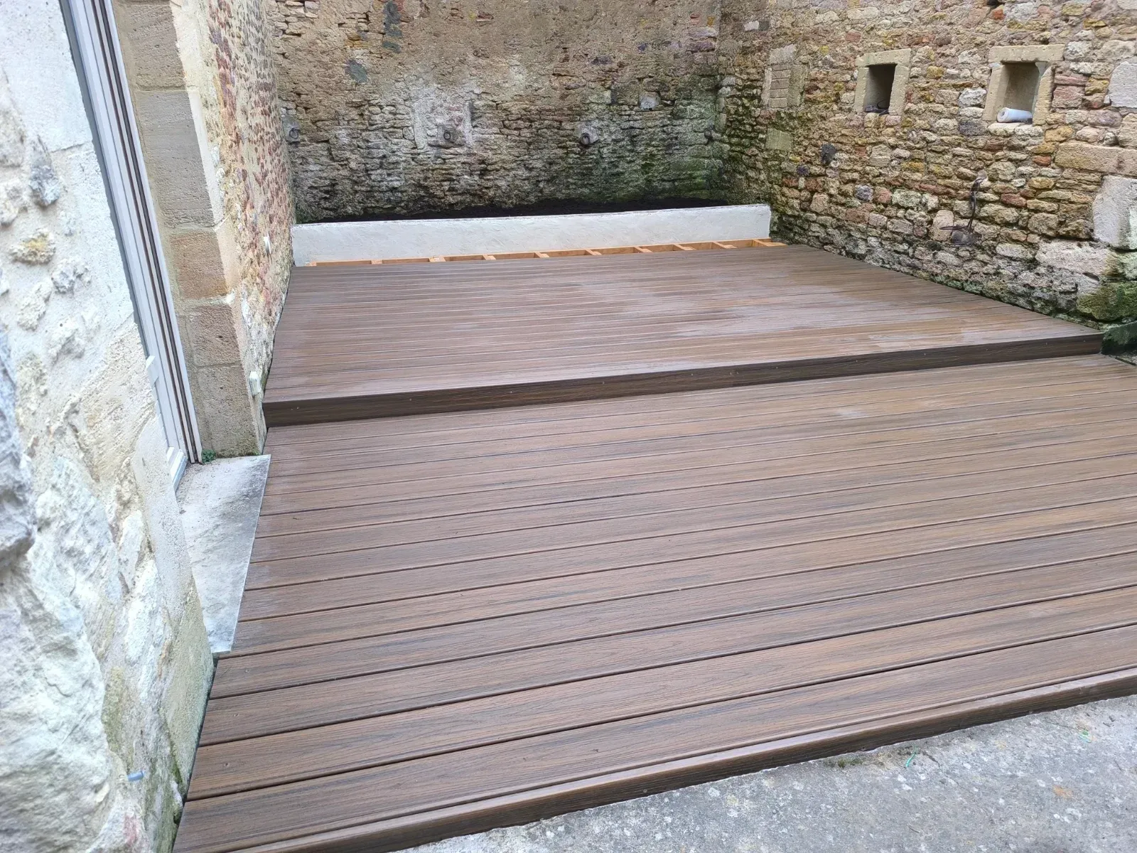 Terrasse en lames composite dans une cour en pierre de taille