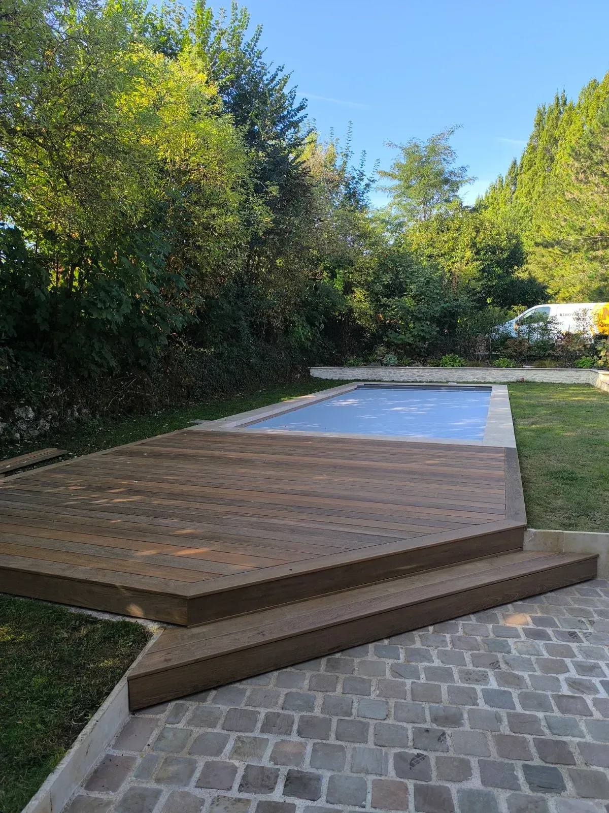 Marches en bois exotique entre une plage de piscine et une cour pavée