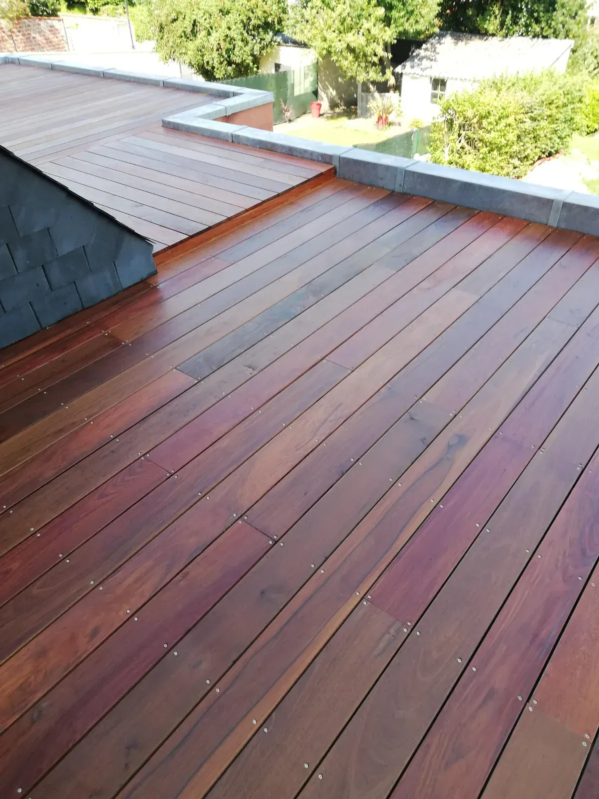 Terrasse en bois exotique rénovée et saturée sur un toit-terrasse, lames rouges profondes