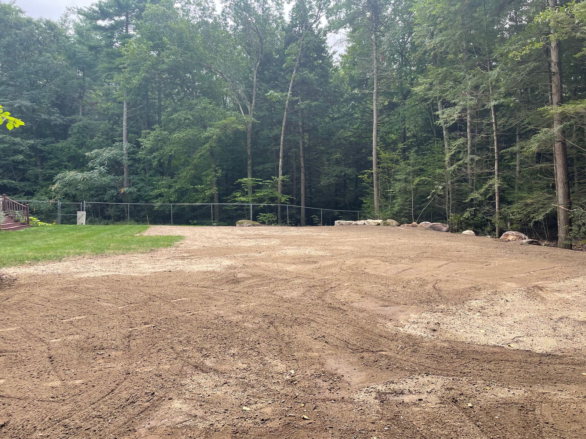 Cleared dirt area with a chain link fence, green grass, and trees in the background.