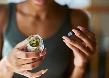 Person holding a small jar of green cannabis.