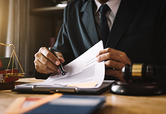 Lawyer in suit signing document; scales of justice, gavel, and books on desk.