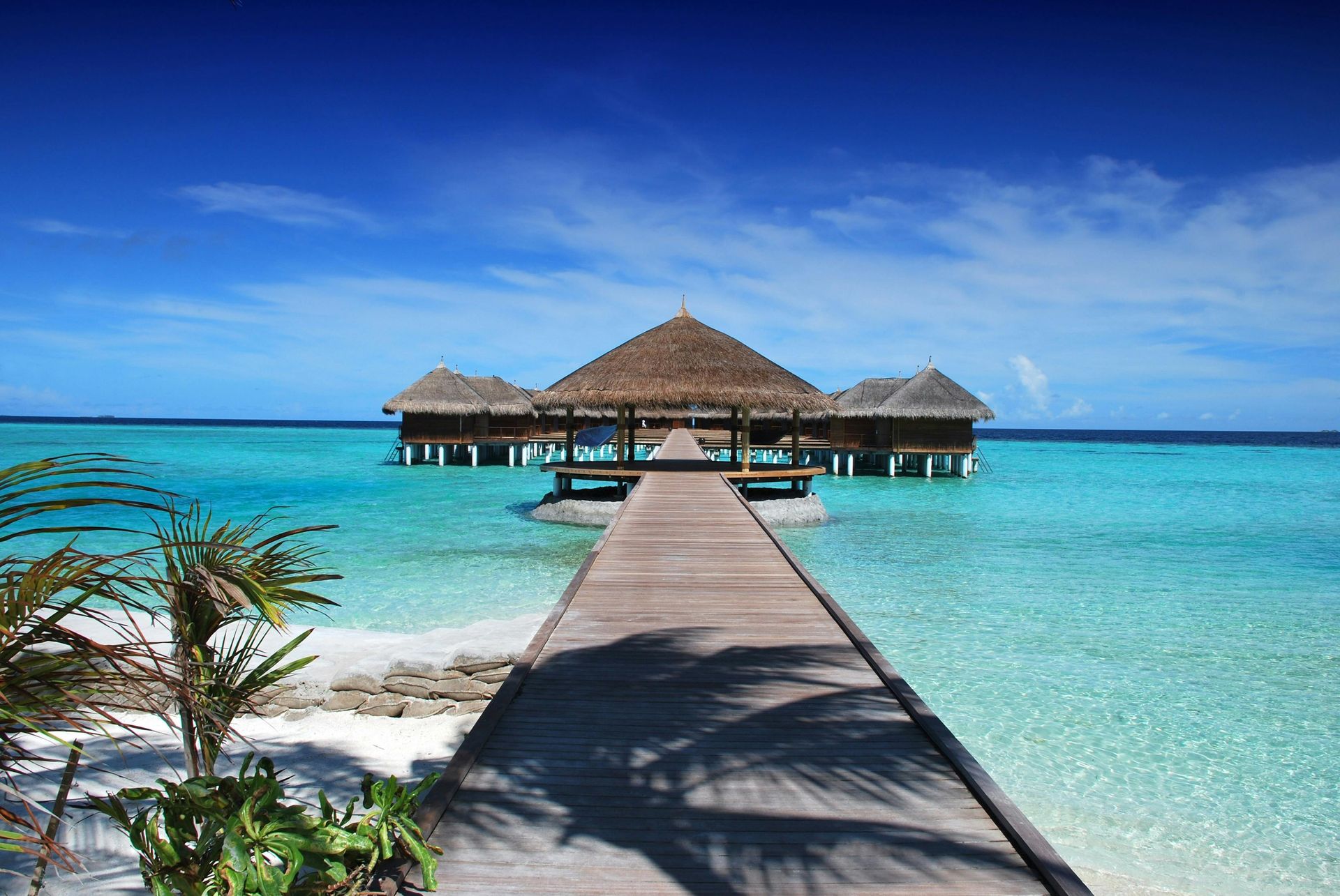 Wooden walkway leads to overwater bungalows in turquoise water under a blue sky.