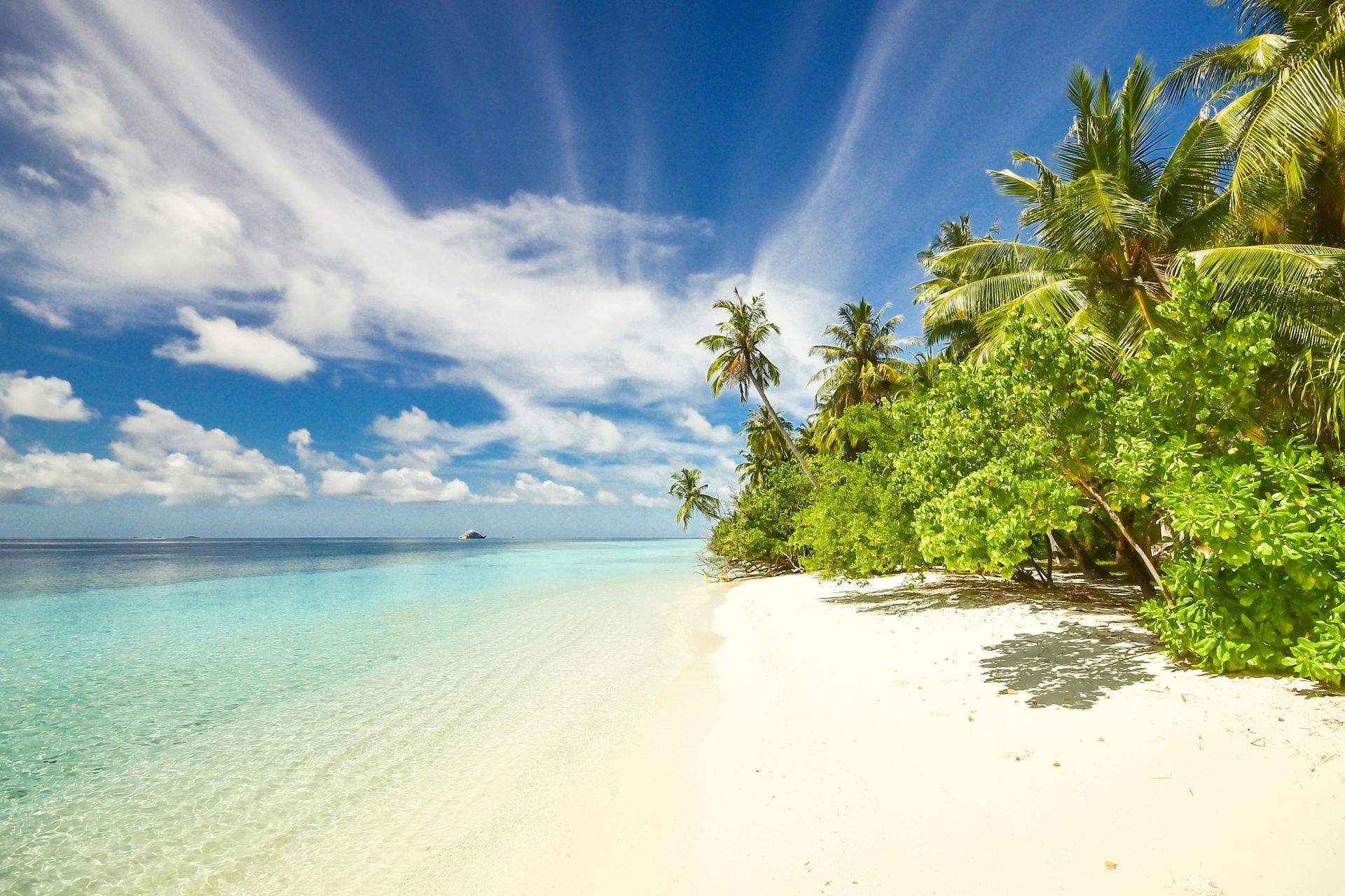 Tropical beach with white sand, turquoise water, palm trees, and blue sky with clouds.