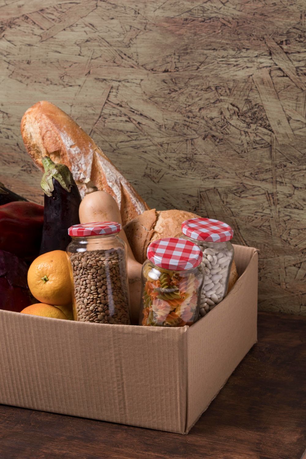 Una caja de cartón llena de una barra de pan, fruta y frascos de cereales y especias.