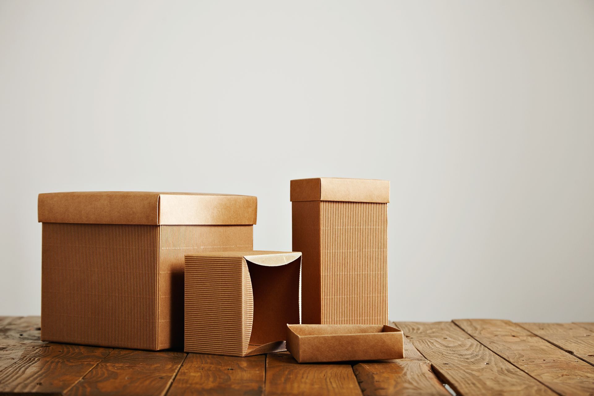Cuatro cajas de cartón corrugado de diferentes tamaños se encuentran sobre una superficie de madera contra un fondo neutro.