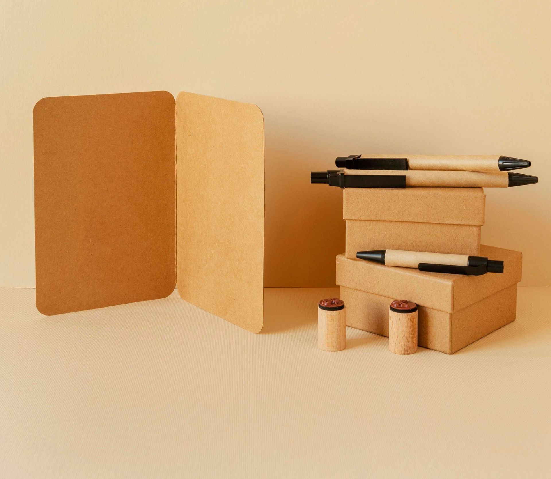Juego de papelería marrón sobre una superficie beige claro. Incluye una tarjeta, cajas apiladas, bolígrafos y sellos.