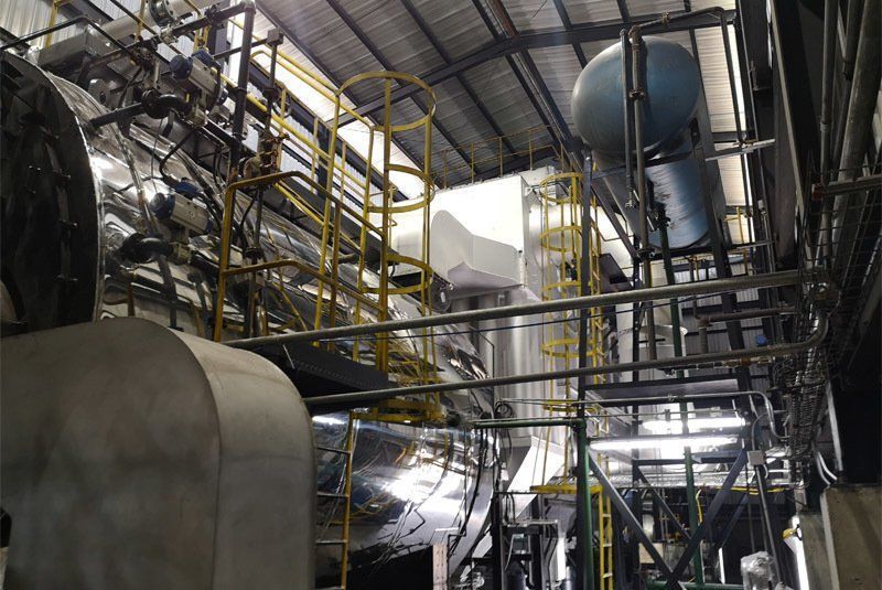 Interior industrial con tuberías metálicas, tanques y barandillas de seguridad amarillas; una luz brillante brilla desde una abertura en la estructura.