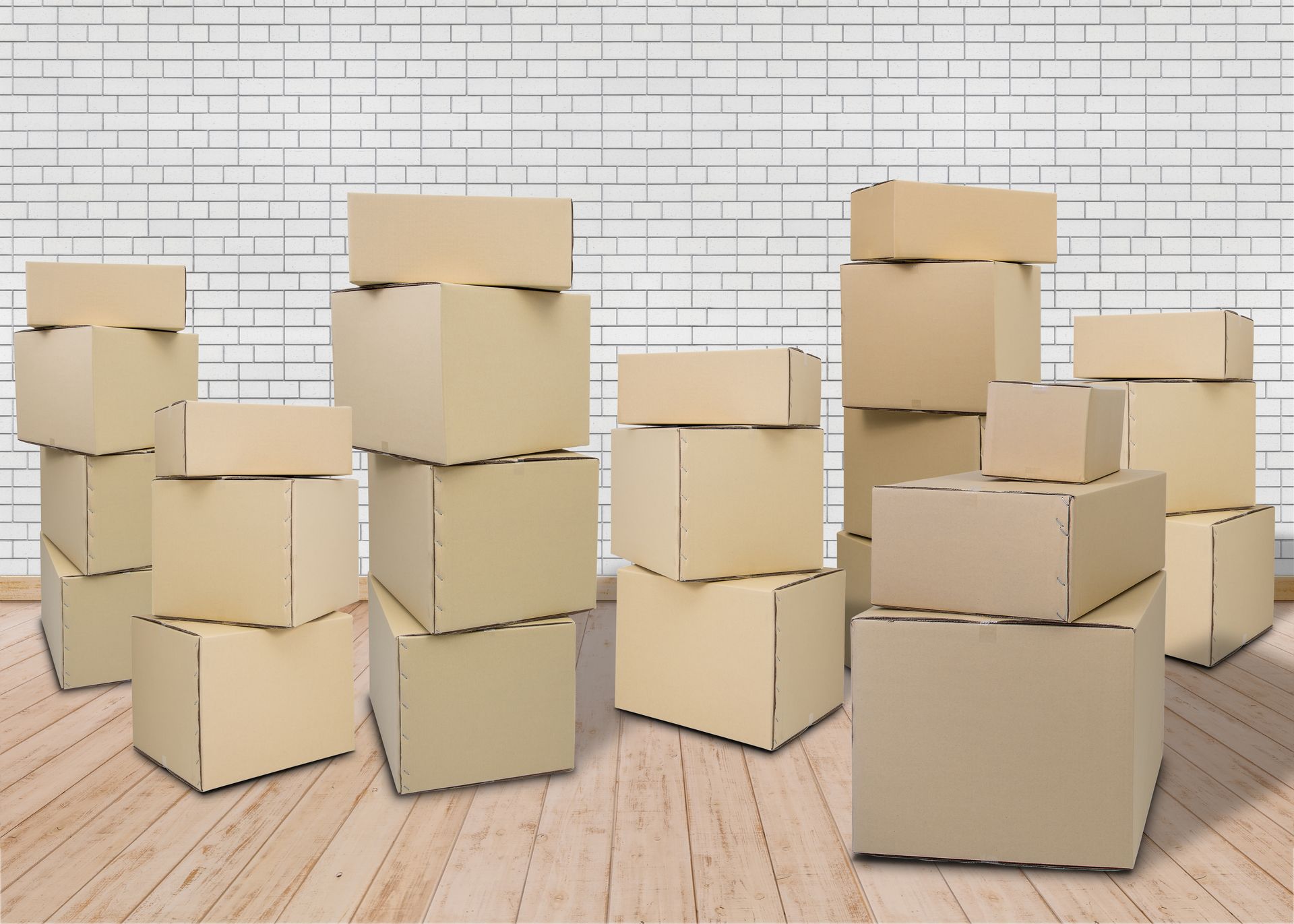 Cajas de cartón al por mayor apiladas en una habitación con piso de madera y pared blanca.