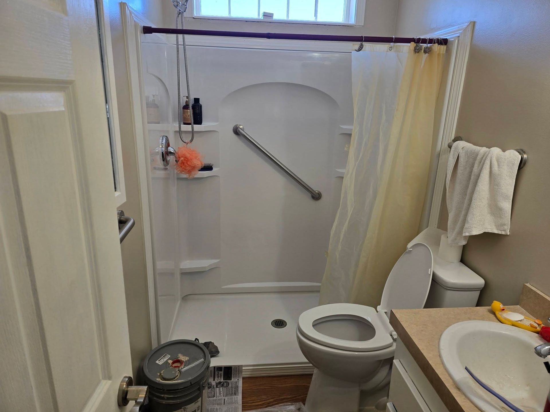 A small bathroom with a white walk-in shower stall featuring a grab bar, a toilet, and a vanity sink.