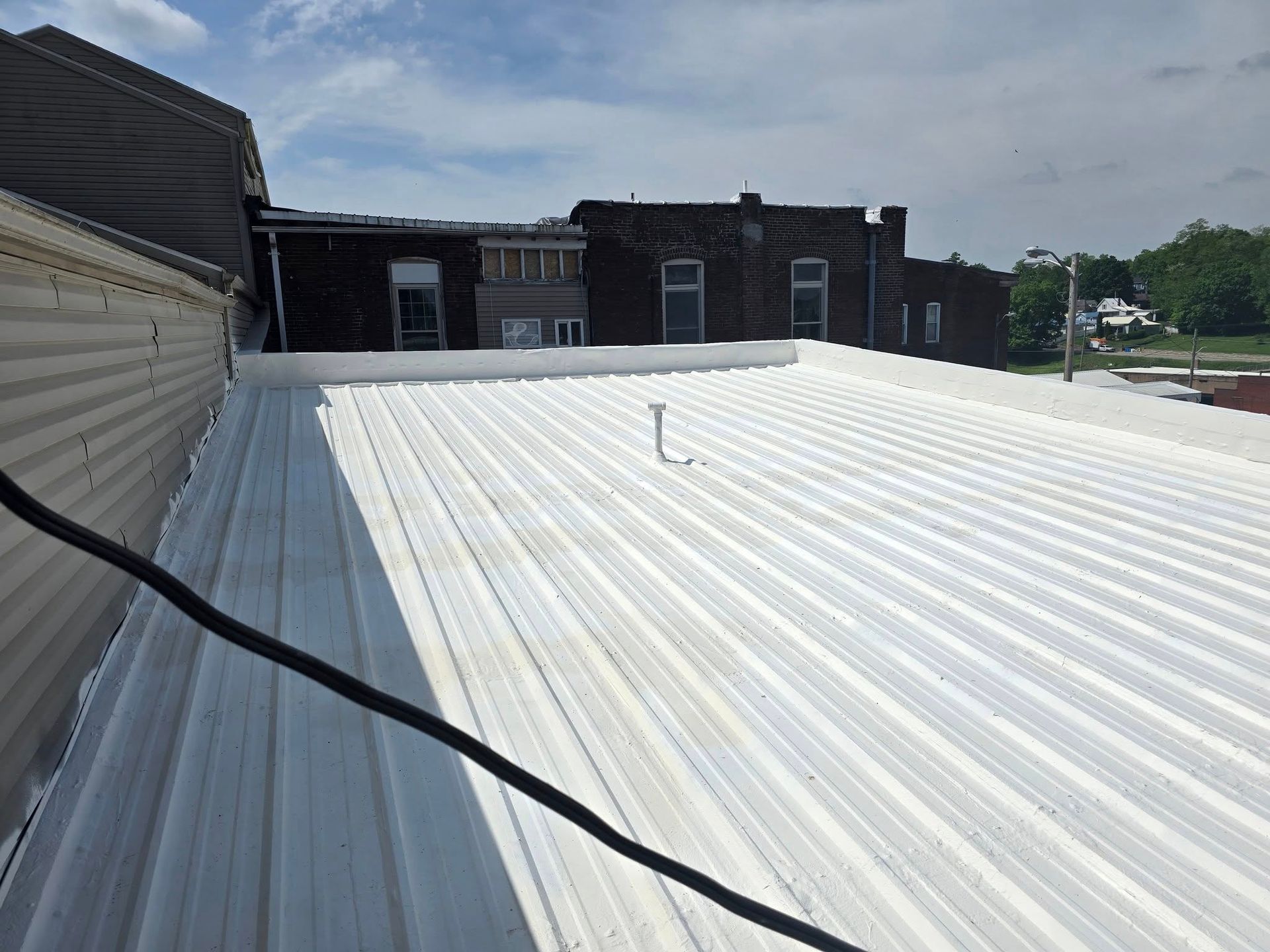 A white metal roof surface with a small vent pipe, viewed from a slightly elevated angle against a dark building facade.