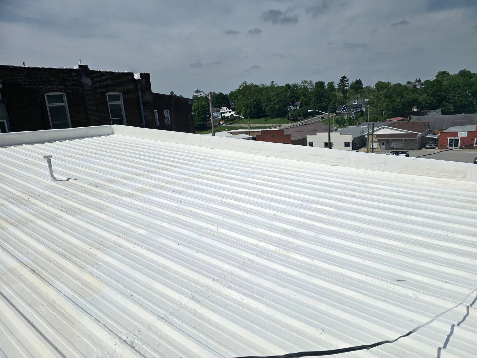 A view from a roof showing a white, corrugated metal roof surface with a dark brick building and town in the background.