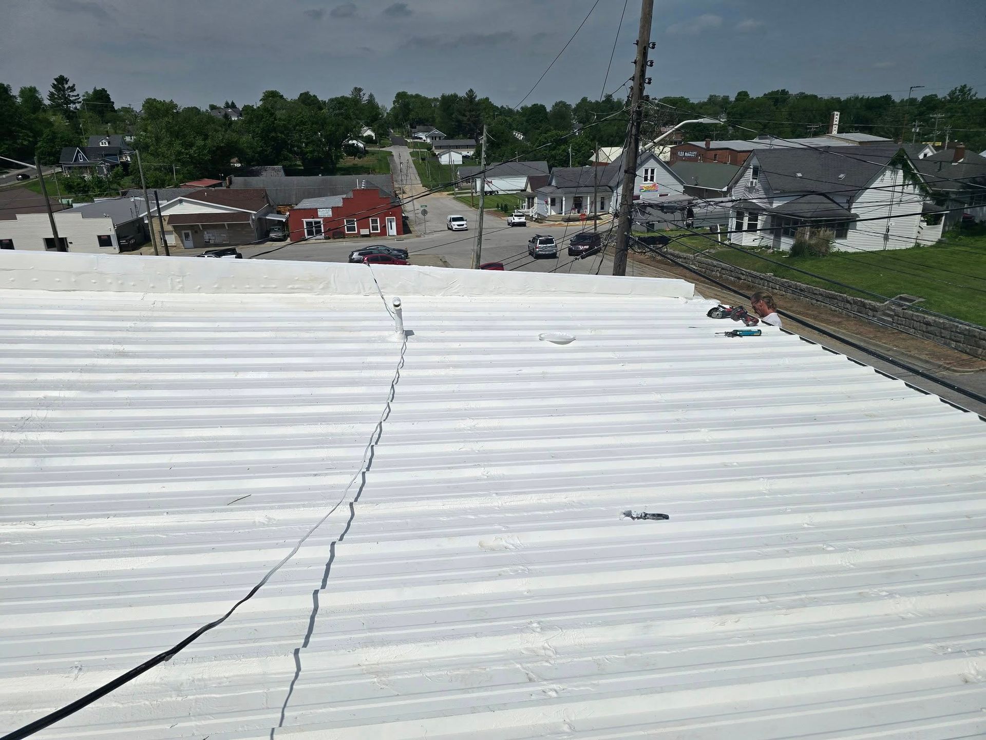 A view from a white metal roof overlooking a town street with houses and trees under a cloudy sky.