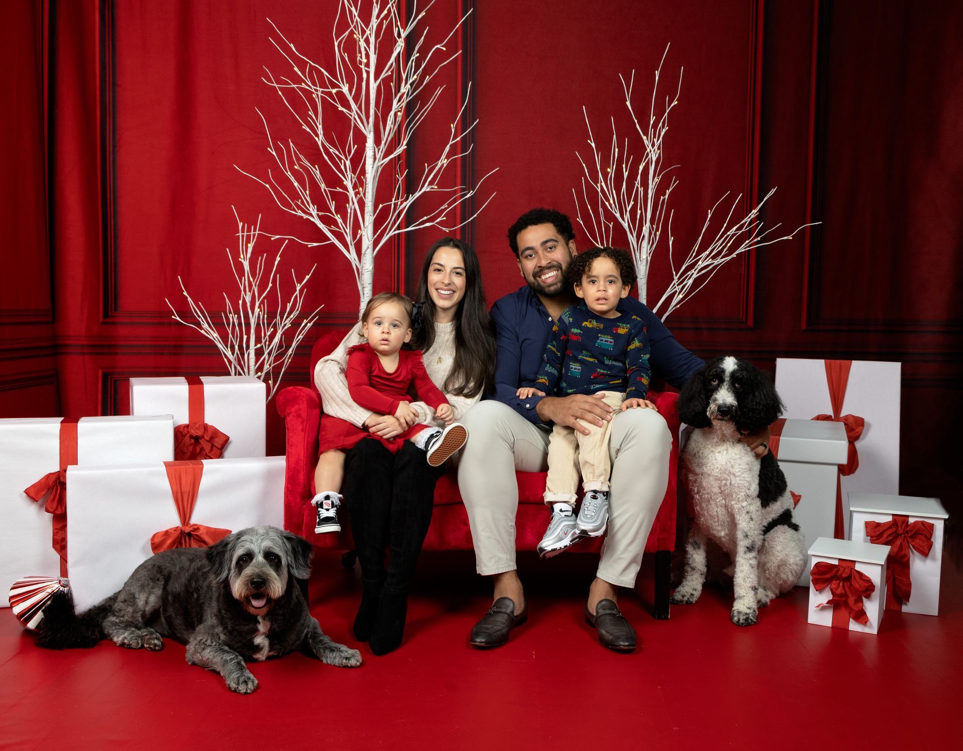 A family is sitting on a red couch with two dogs.