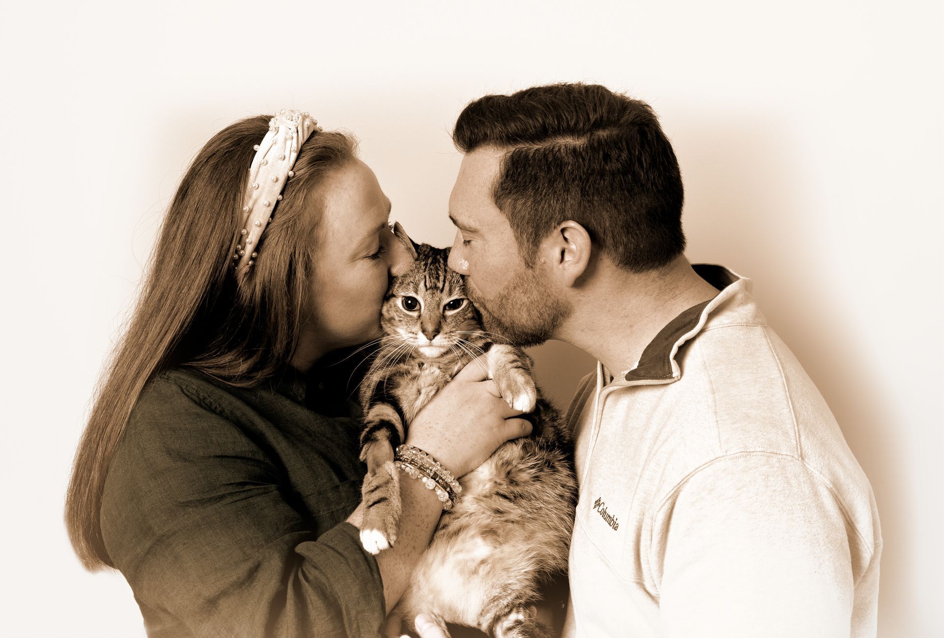 A man and a woman are kissing a cat on the nose.