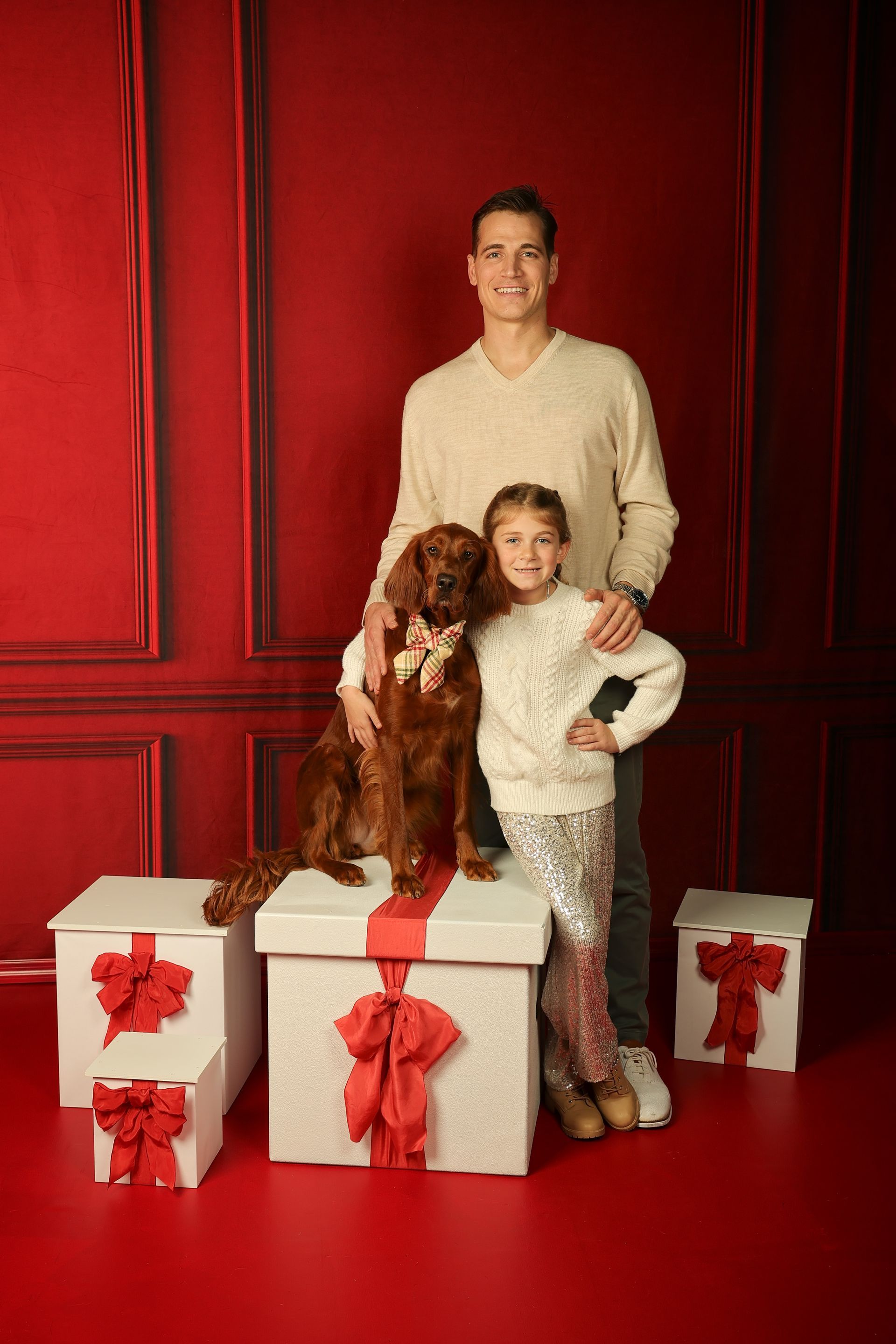 A father and daughter are posing for a Christmas portrait with their dog.