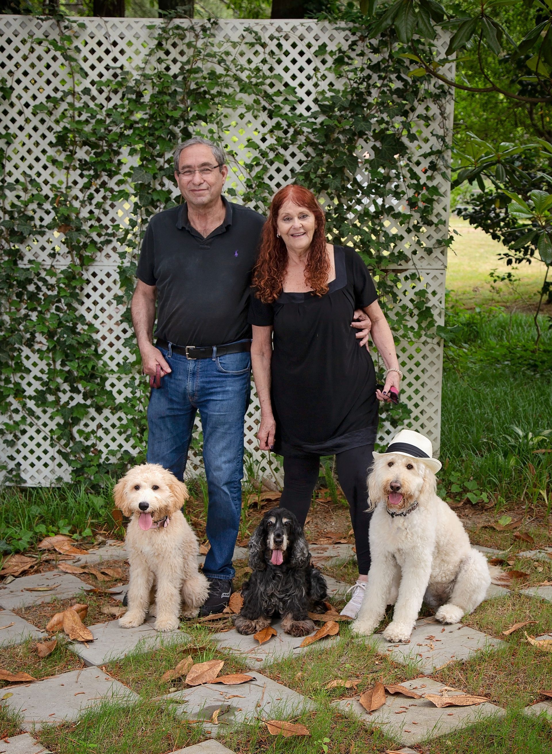 A man and a woman are posing outside for a portrait with their dogs.