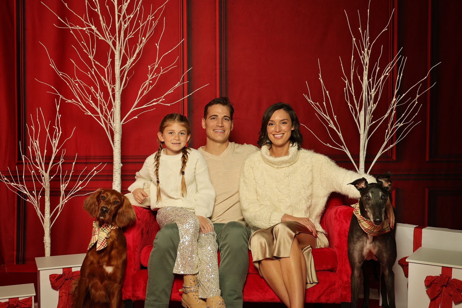 A family is sitting on a red couch with their two dogs.