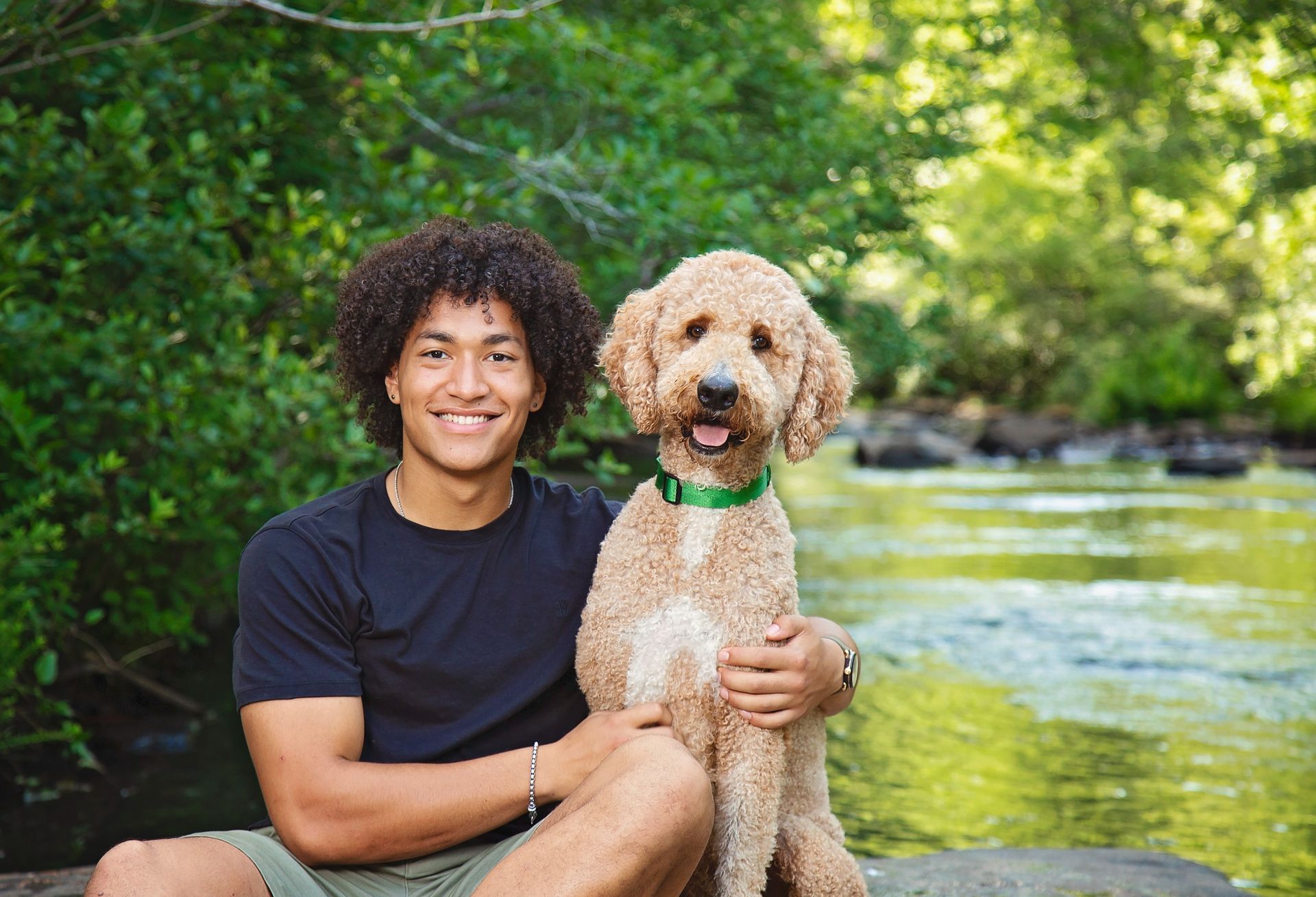 A young man is sitting on a rock holding a dog.