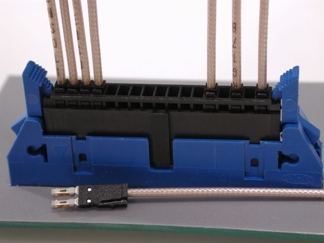 Blue and black electrical connector with wires, resting on a reflective surface, with a cable and connector.