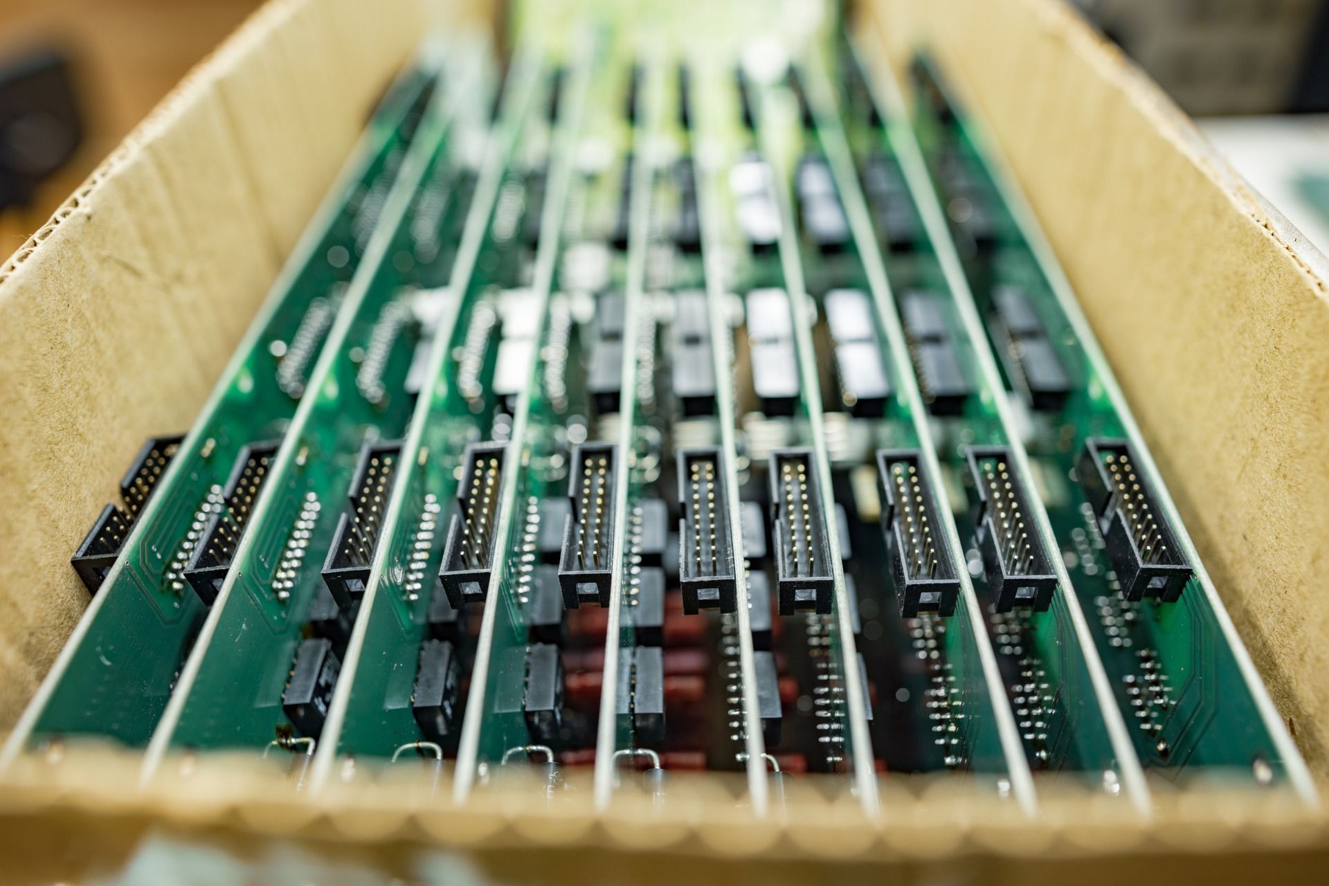 Circuit boards stacked in a cardboard box, green with black connectors and components.