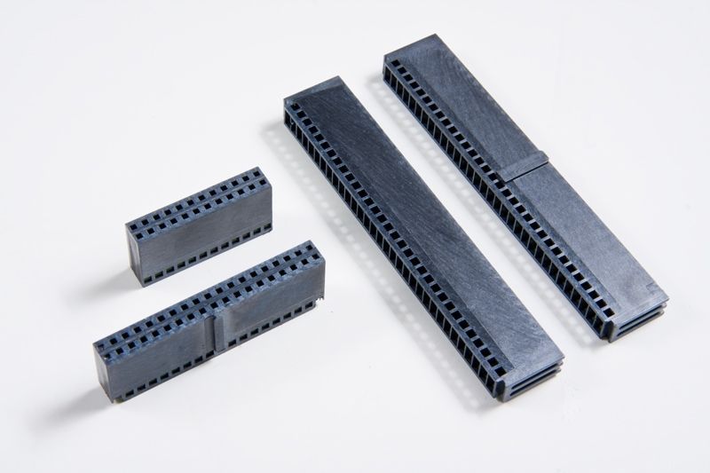 Black electronic connector pins, in multiple sizes, on a white surface.