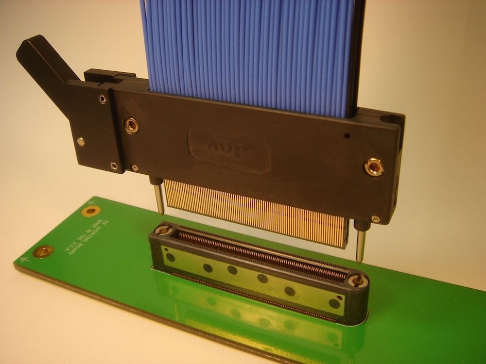 A black tool aligning blue wires above a green circuit board with a connector.