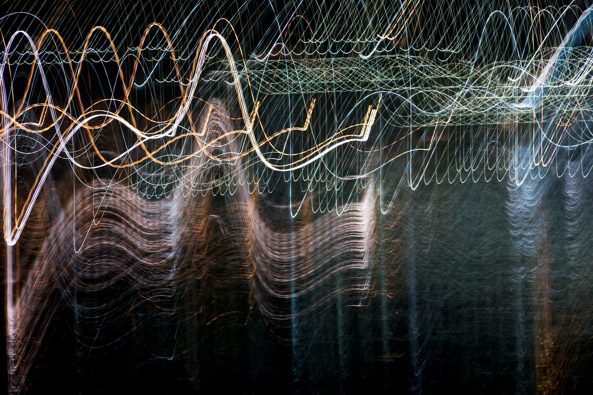Abstract light trails in white, gold, and blue against a dark background, creating a wavy, blurred pattern.