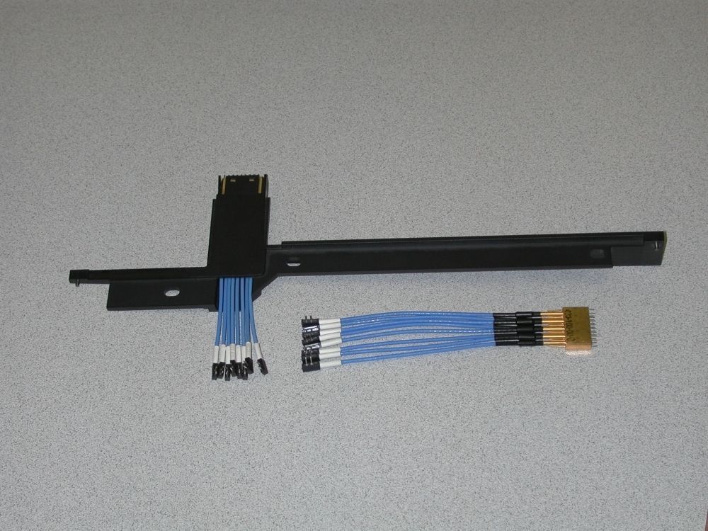 A black connector with blue and white wires and a gold connector, laid out on a light grey surface.