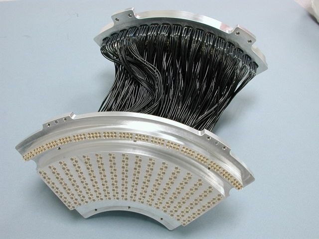Arc-shaped electronic connector with numerous wires, metallic frame, and small gold-colored pins.