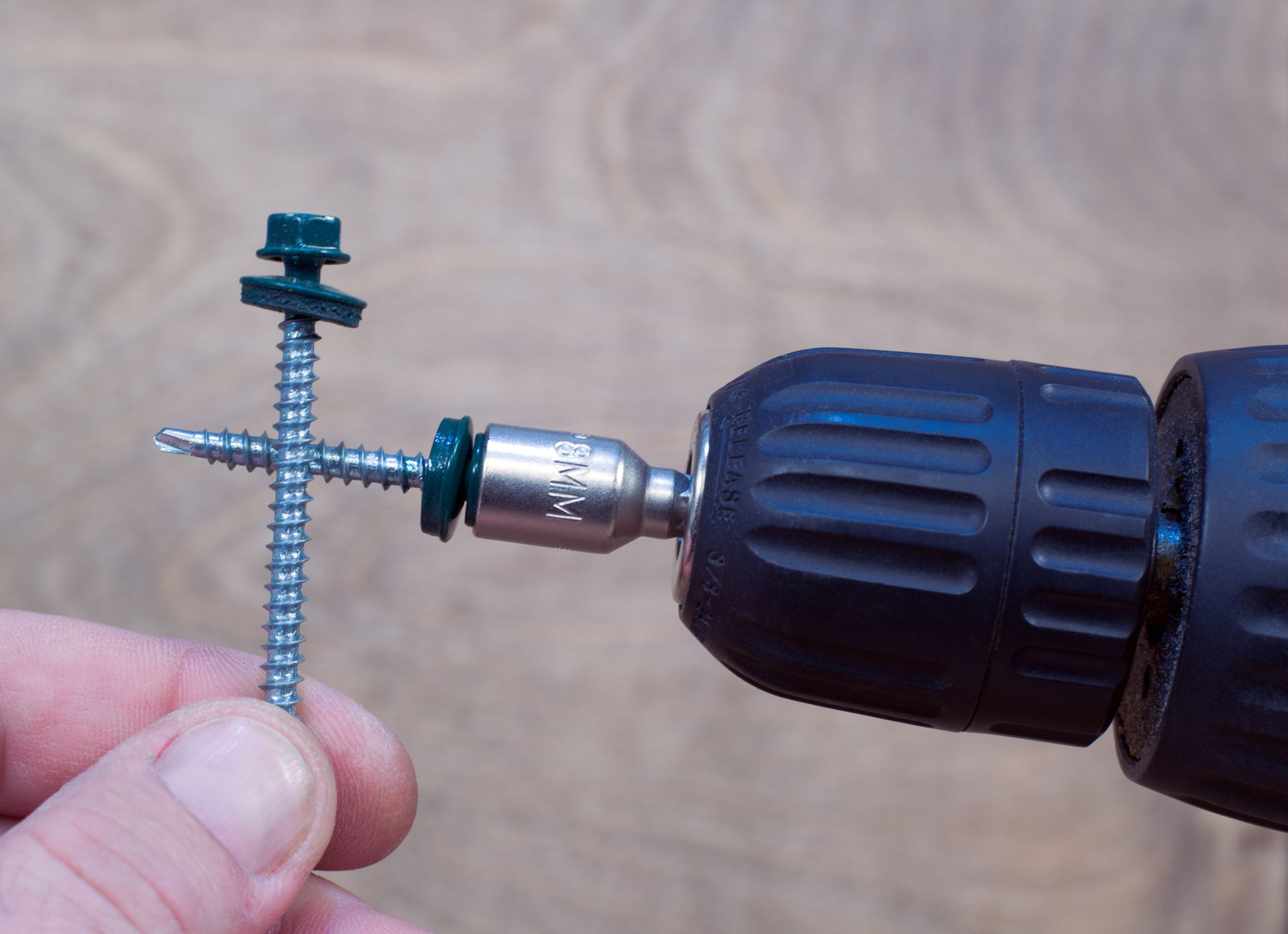 A person is holding a screw and a drill in their hand.