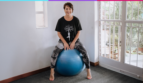 Person sitting on a blue exercise ball in a bright room by a window.