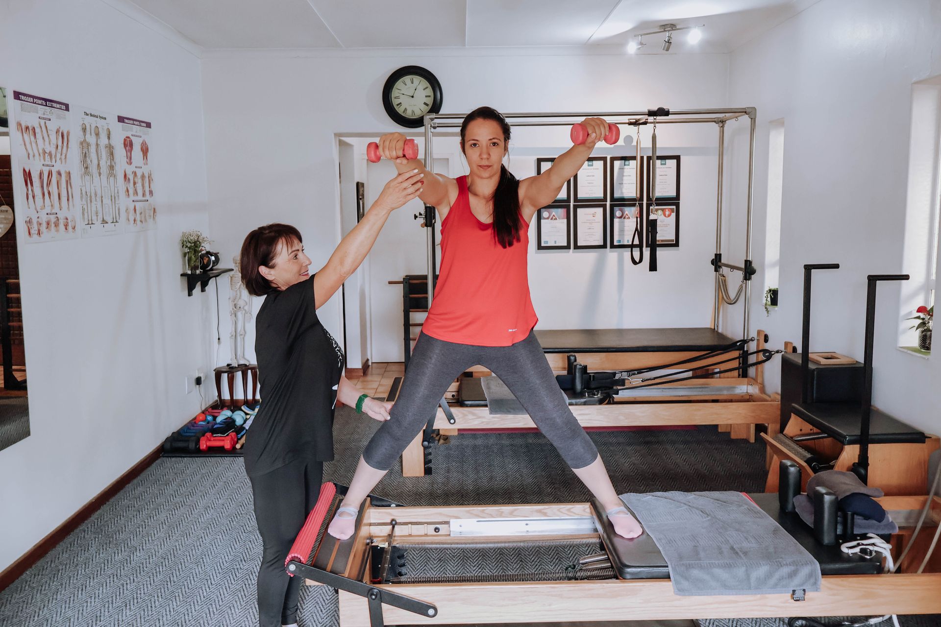 Woman exercising on a Pilates reformer as a trainer assists in a studio.